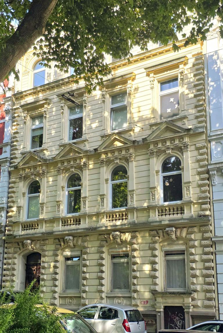 Die prachtvolle Fassade eines historischen Altbaus mit zahlreichen Fenstern, teilweise verdeckt von einem großen Baumbestand.